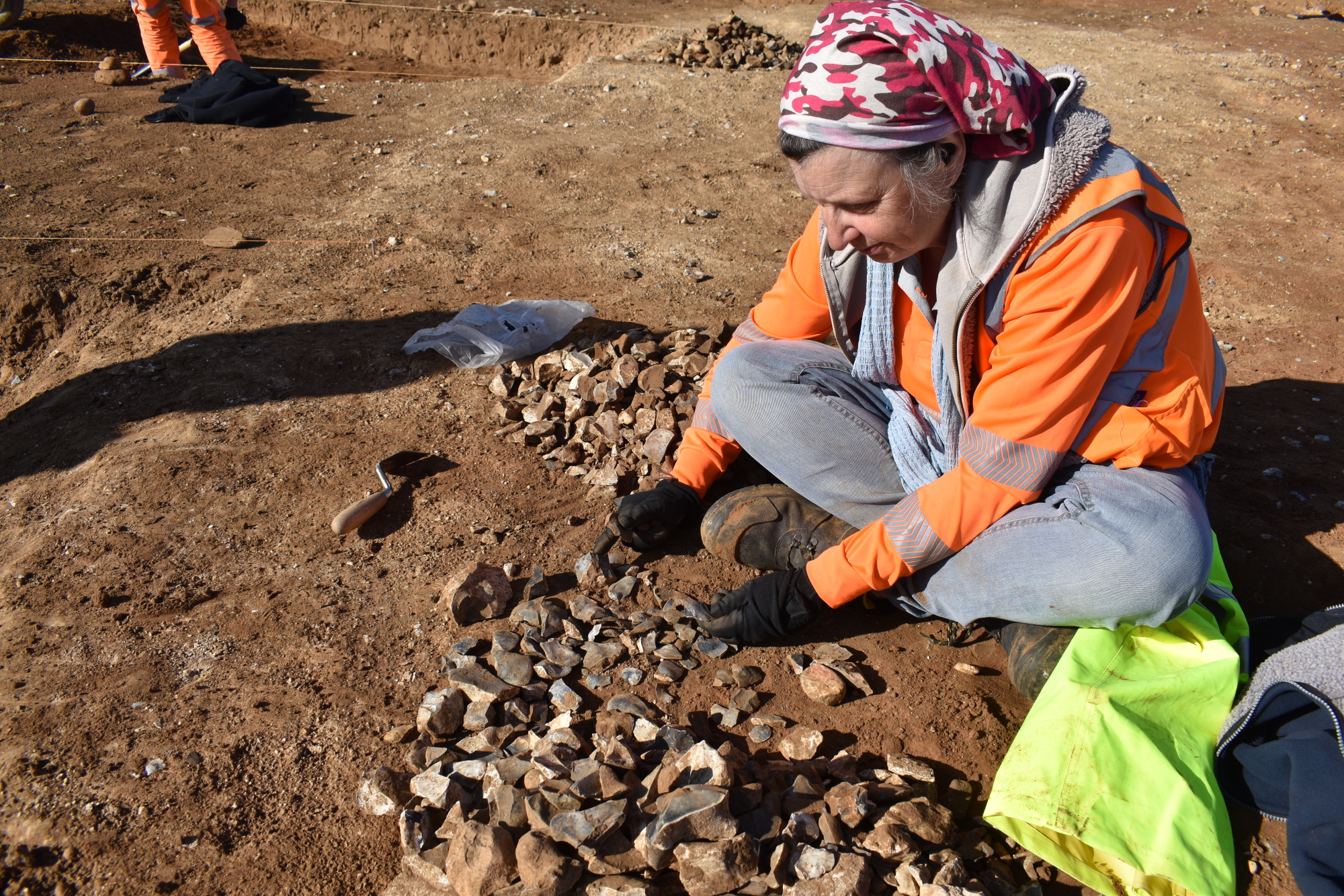 An archaeologist sits cross legged surrounded by worked flints which she is checking.