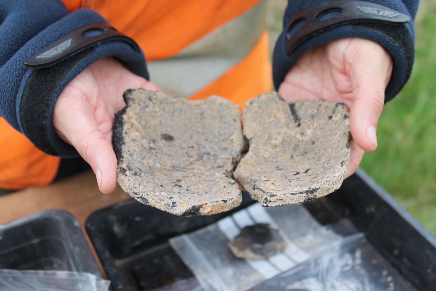 An archaeologist holds two pieces of broken muddy pottery.