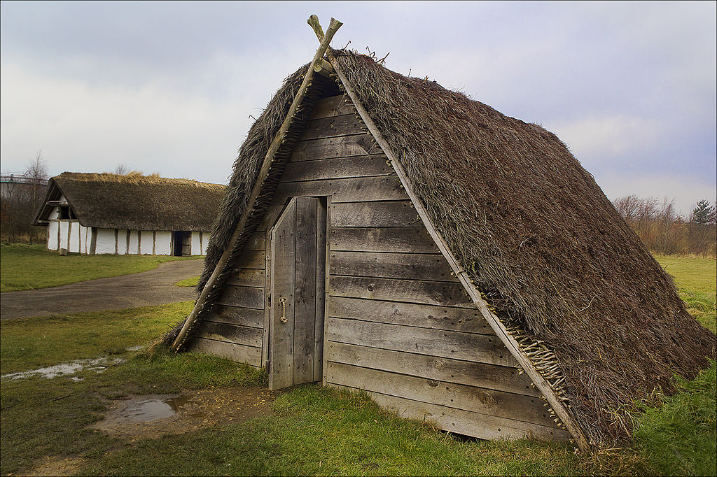 A reconstruction of an Anglo-Saxon sunken feature building. It is triangular in shape, with a thatched roof that reaches to the ground.