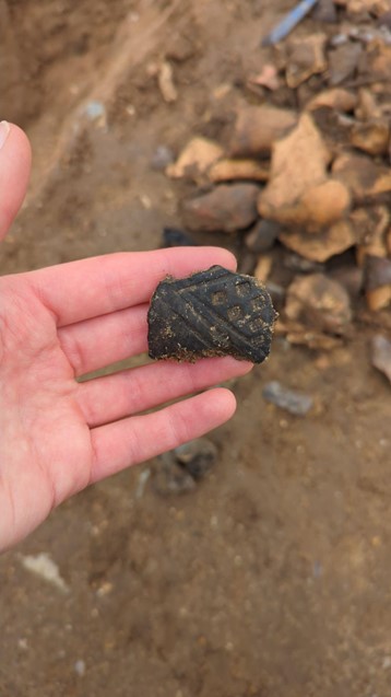 Hand holding sherd of black, decorated pottery