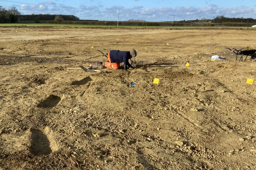 An archaeologist bends down to excavate the ditch of an Iron Age roundhouse