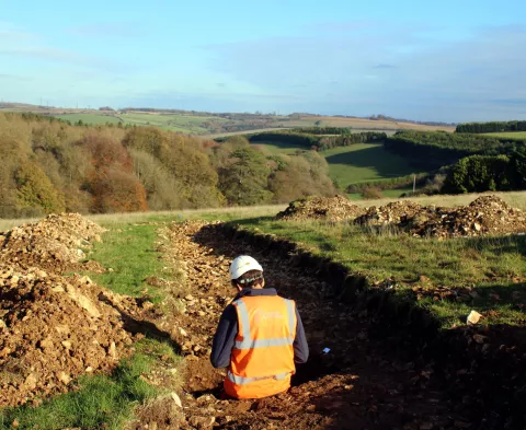 archaeologist is recording an evaluation trench while overlooking rolling hills