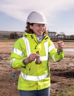 An archaeologist wearing hi-vis and a hard hat holding up finds