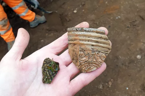 A close up of an archaeologists hands holding two fragments of decorated Medieval pottery