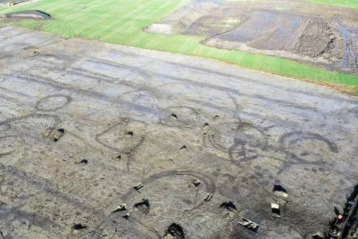 An aerial drone image of roundhouses and enclosure features visible in a field