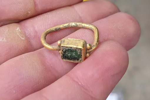 A close up of a hand holding a slightly bent gold Roman ring