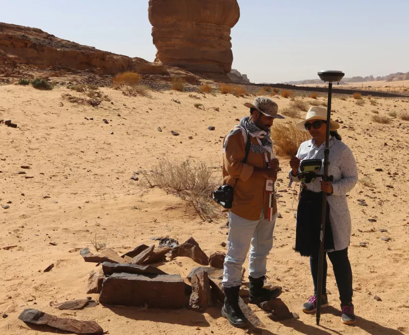 two archaeologist are standing in a desert landscape surveying