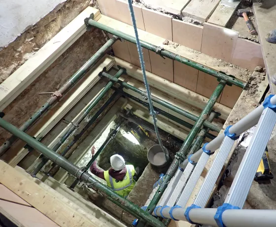 An archaeologist works in a deep excavation inside the building