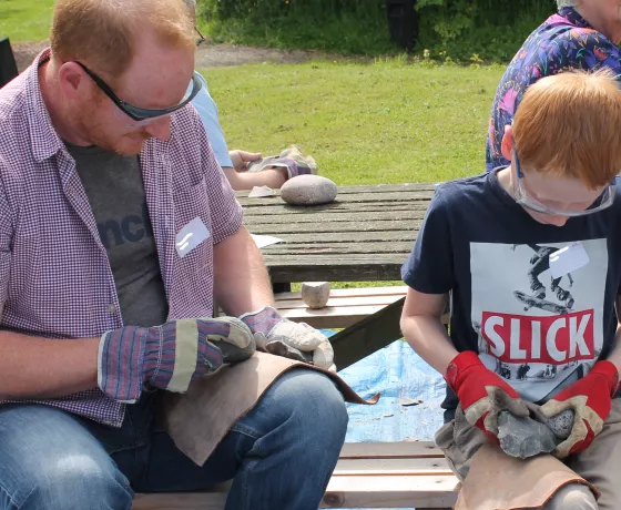 An adult and child learning to knap flint.