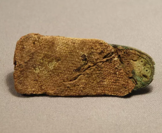 A copper-alloy strap end from Grave 2 preserving the remains of textiles from the clothing or burial goods. 